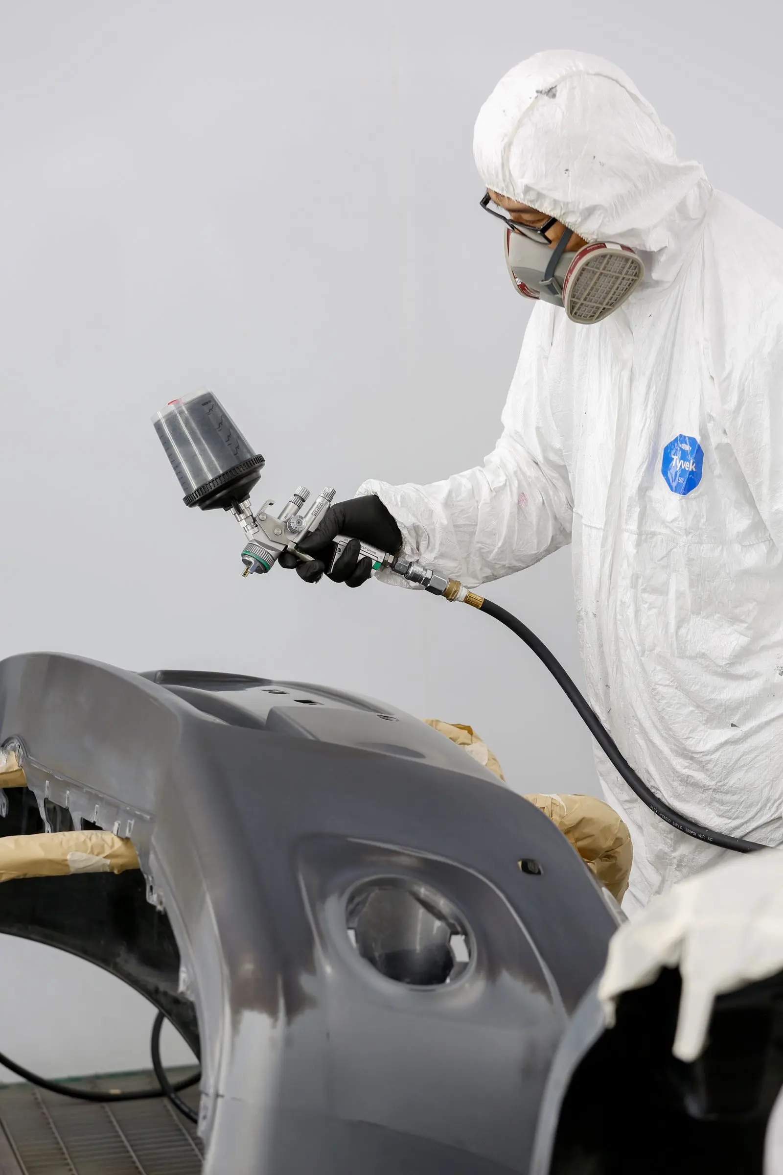 Técnico con equipo de protección aplica pintura a una pieza automotriz dentro de una cabina